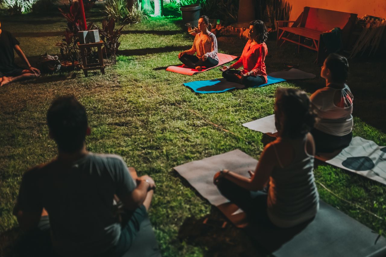 social-feed-img-04 A group of adults practicing yoga outdoors at night on mats in a serene garden setting.