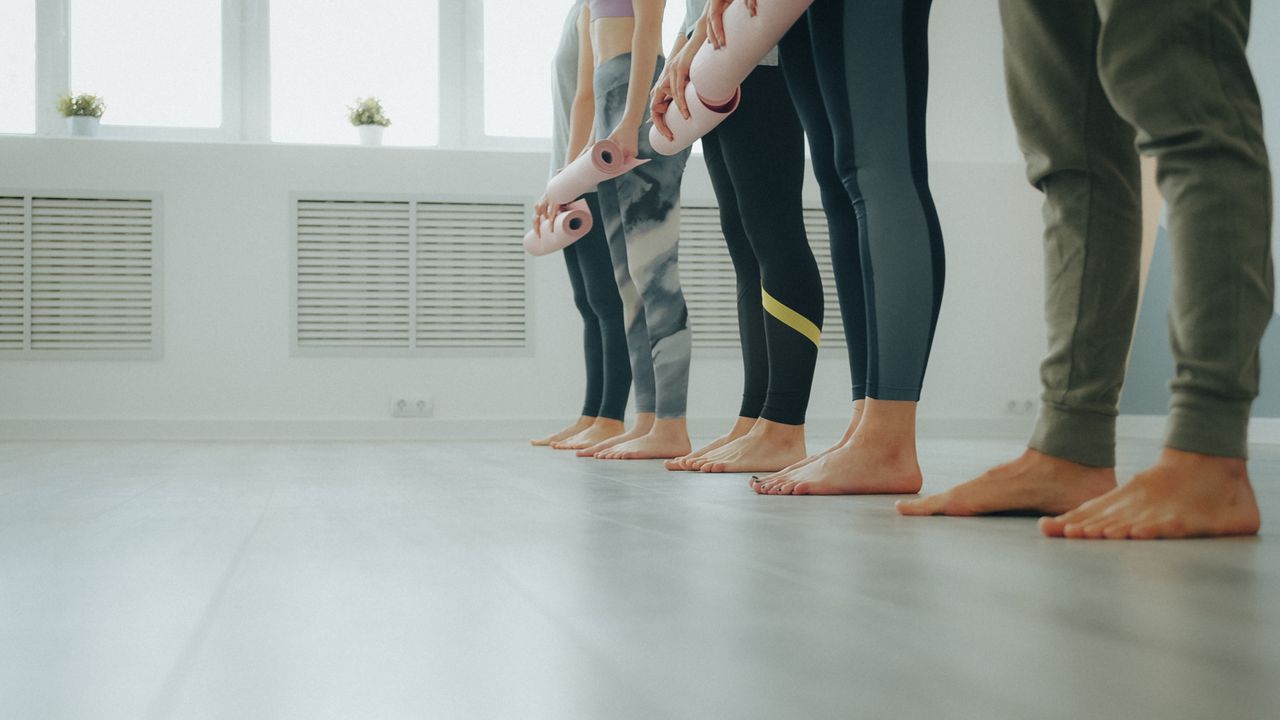 social-feed-img-04 A group of people in leggings ready for a yoga class in a bright studio.