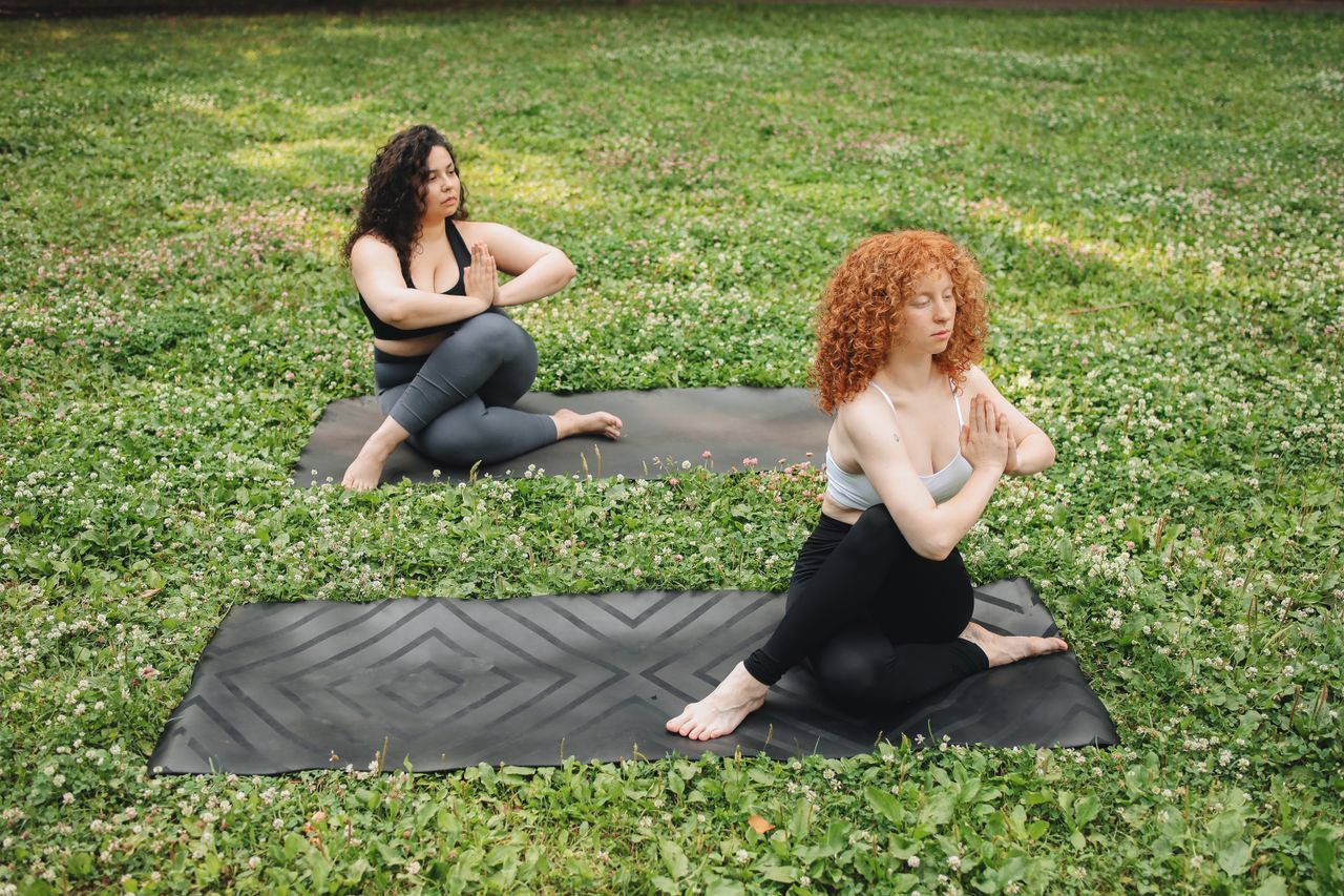 quality-assurance-01 Two women practicing yoga in a tranquil outdoor setting, surrounded by lush grass.